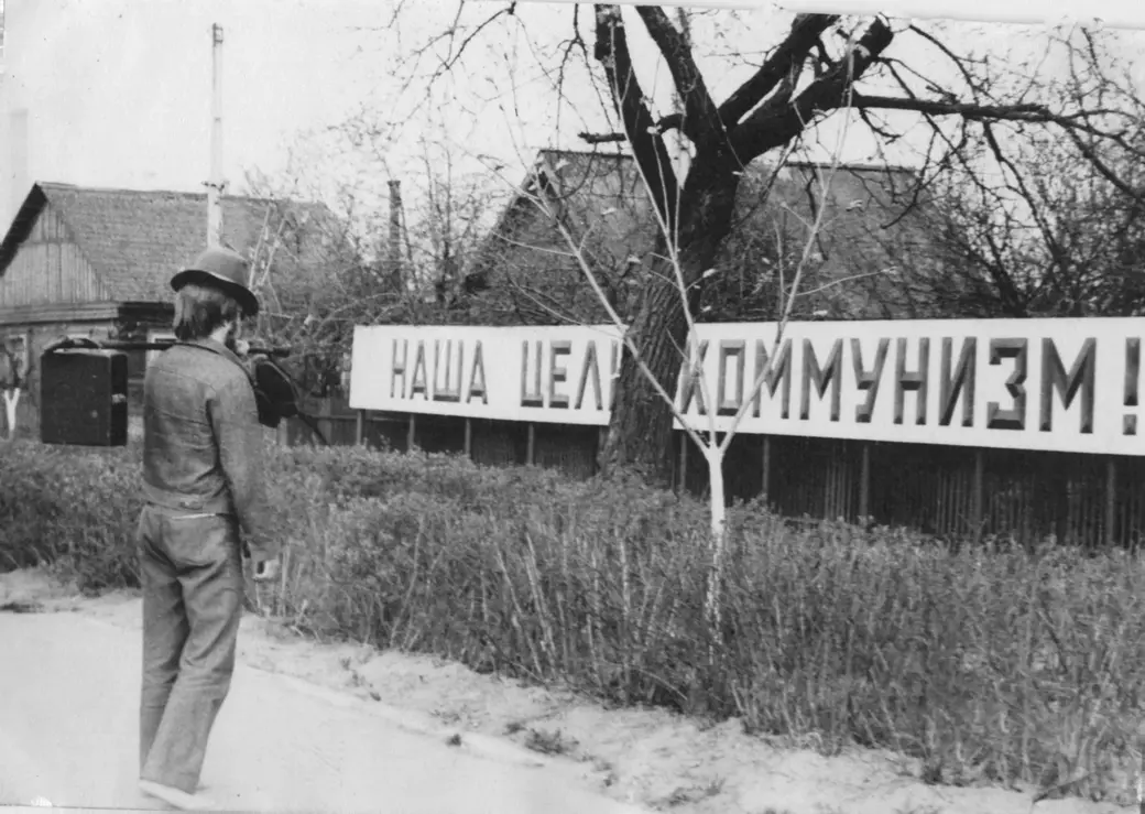 Саша Образцов, с почтением разувшись и повесив туфли на свой посох, внимательно изучает текст недавно появившегося транспоранта. Могилев, улица Челюскинцев, первая