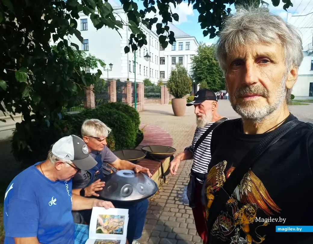 Август 2025 года, Могилев, ул. Ленинская. Борис Борщ слушает необычную музыку, а люди рассматривают альбом его живописных произведений.